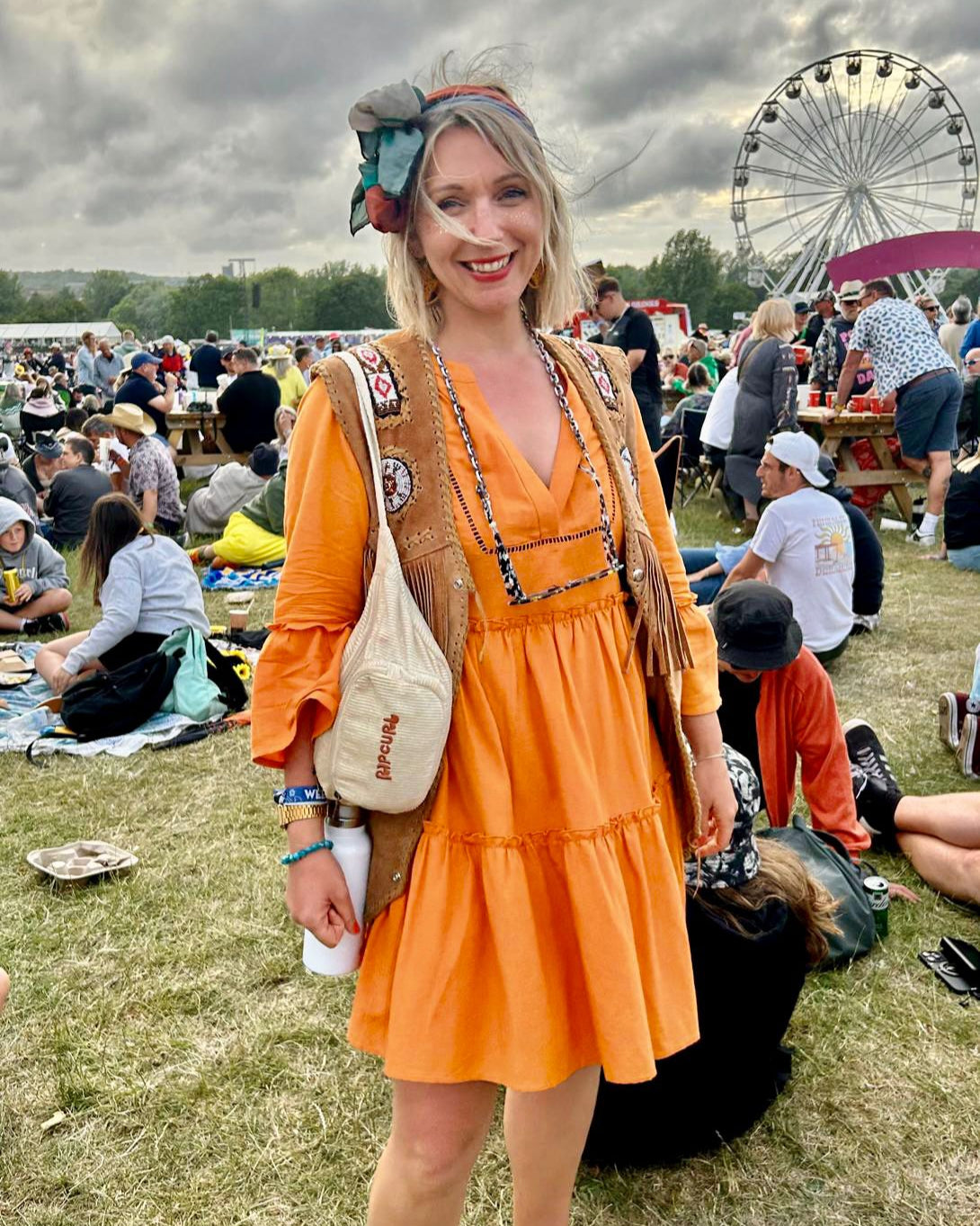 Woman in an orange dress at a festival with a Ferris wheel in the background